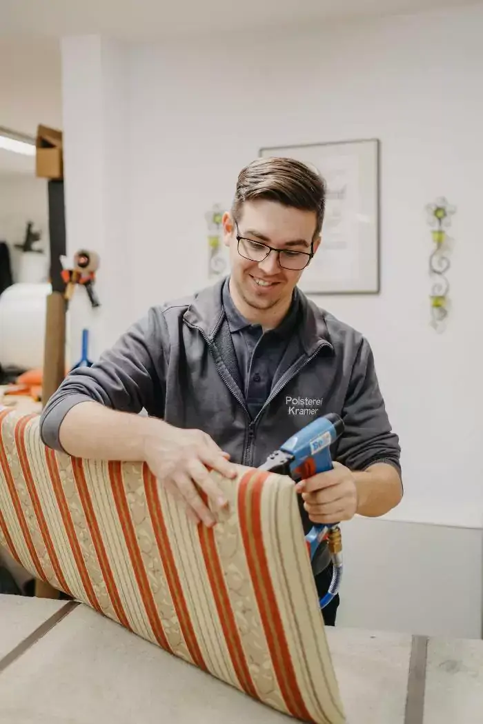 Ein Mitarbeiter bezieht eine Sitzfläche mit einen gestreiften Stoff