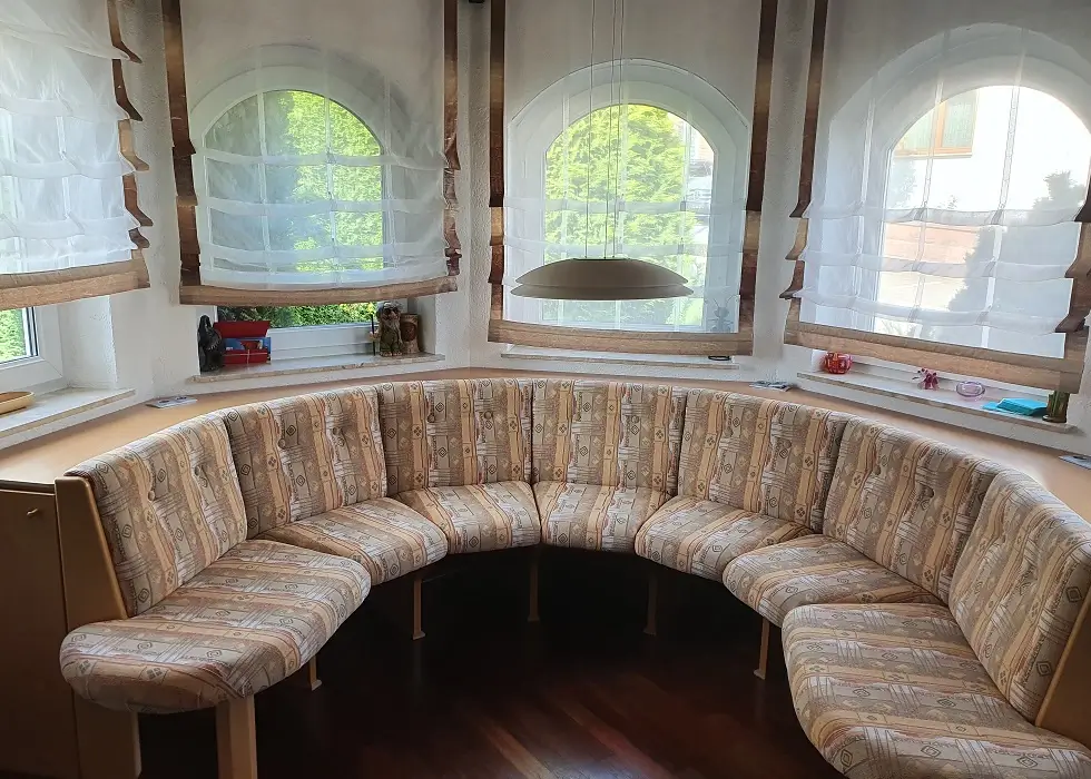 Eine große Eckbank aus Holz mit Polsterung steht in einem Fenstererker.