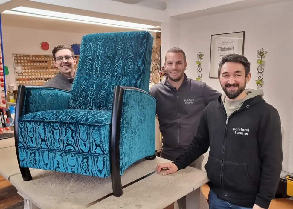 Drei Mitarbeiter und ein blauer Sessel stehen in der Polsterei.