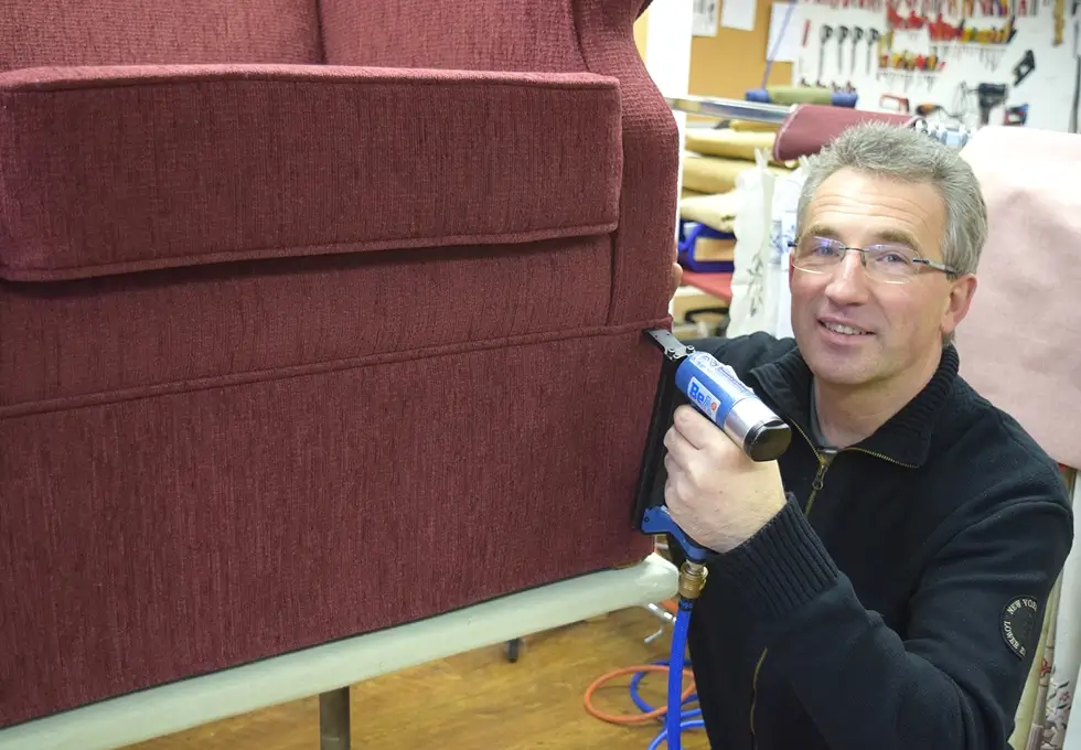 Ein Polstereimitarbieter repariert ein rotes Sofa
